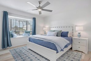 Et soveværelse med seng, natborde, ventilator i loftet og et vindue med gardiner.
