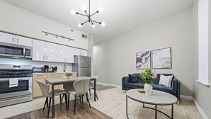 Une cuisine moderne dotée d’appareils électroménagers intégrés, un coin repas avec une table et des chaises, et un espace de vie avec un canapé et une table basse.