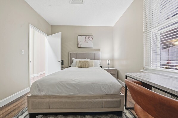 A bedroom with a bed, bedside table, lamp, and a window with blinds. - Home-style 1BR perfect for long visits (New Haven)