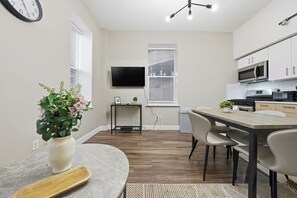 A modern kitchen with white cabinets, a microwave, and a dining area with a table and chairs. - Home-style 1BR perfect for long visits (New Haven)
