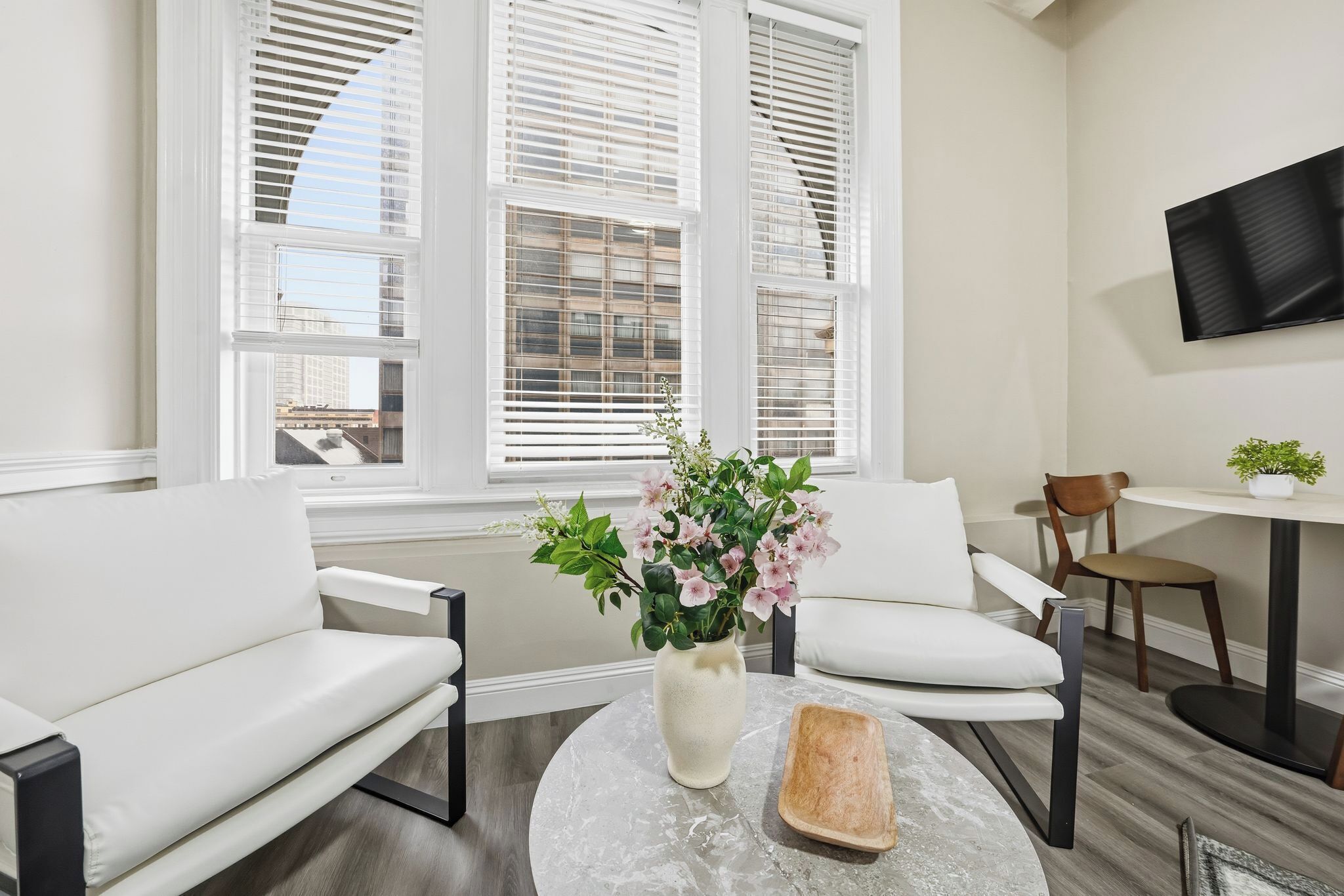 A modern living room with a sofa, a round coffee table, a vase with flowers, and a flat-screen TV mounted on the wall.