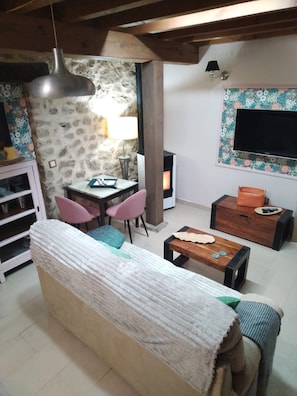 Un salon chaleureux avec un canapé, une table basse en bois, un mur en pierre, une cheminée et un téléviseur fixé au mur.