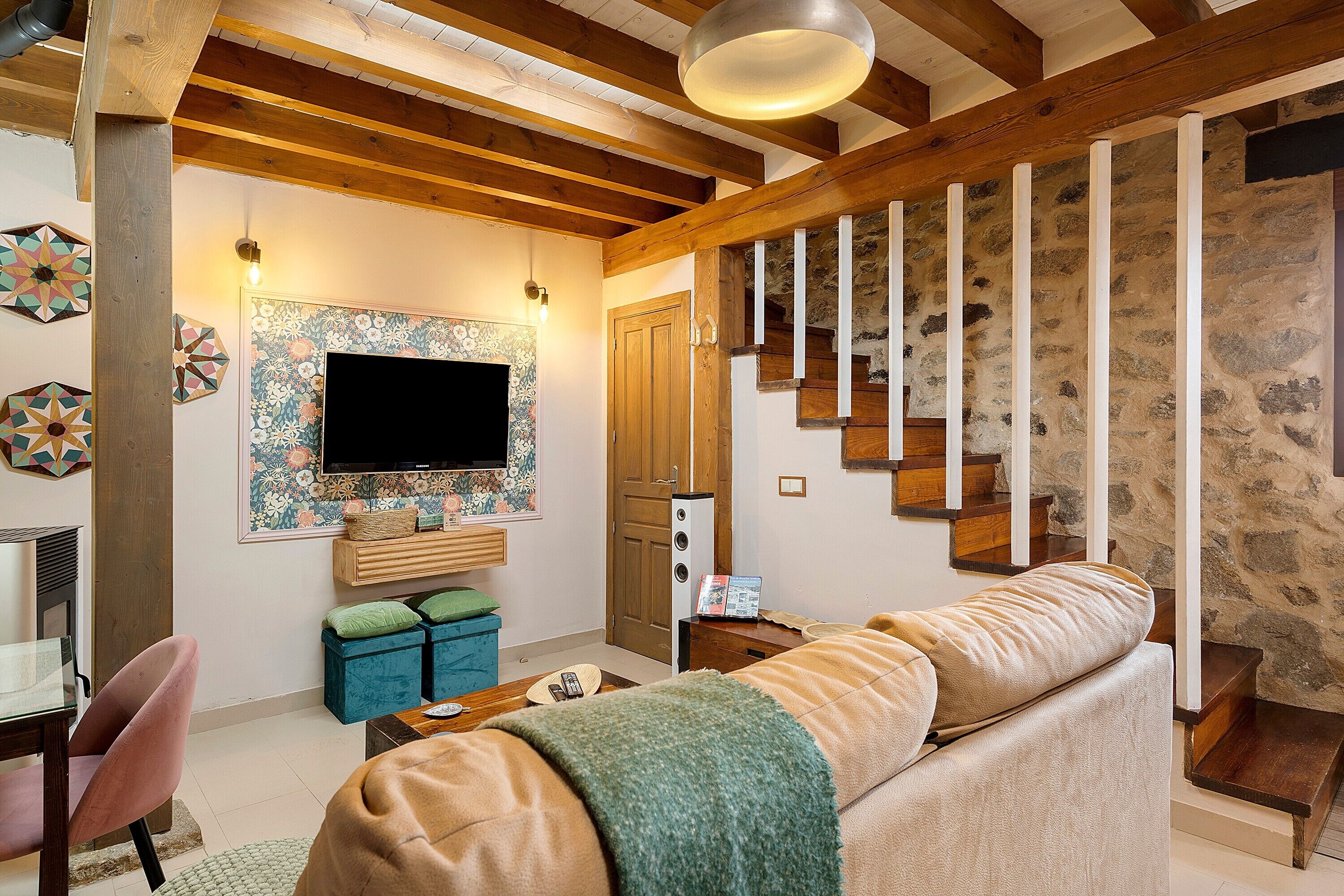 Een woonkamer met een bank, een televisie, een houten trap en een decoratieve wand.