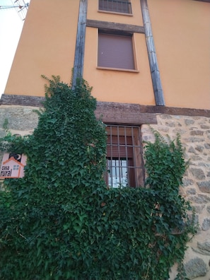 Un bâtiment doté d’une façade en pierre, d’une structure en poutres de bois et d’une fenêtre ornée de barreaux en métal.