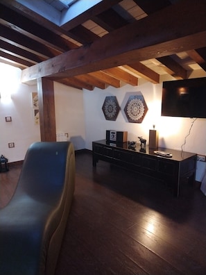 Une pièce dotée d’un parquet en bois foncé, d’un fauteuil en cuir noir, d’un meuble TV noir sur lequel est posé un téléviseur à écran plat, et d’œuvres d’art décoratives accrochées au mur.