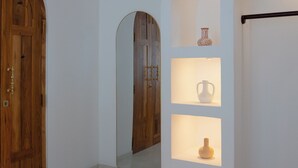Un pasillo con una puerta de madera, un espejo y una estantería con objetos decorativos.