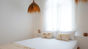Una cama bien tendida con sábanas blancas, dos almohadas decorativas y una lámpara colgante.