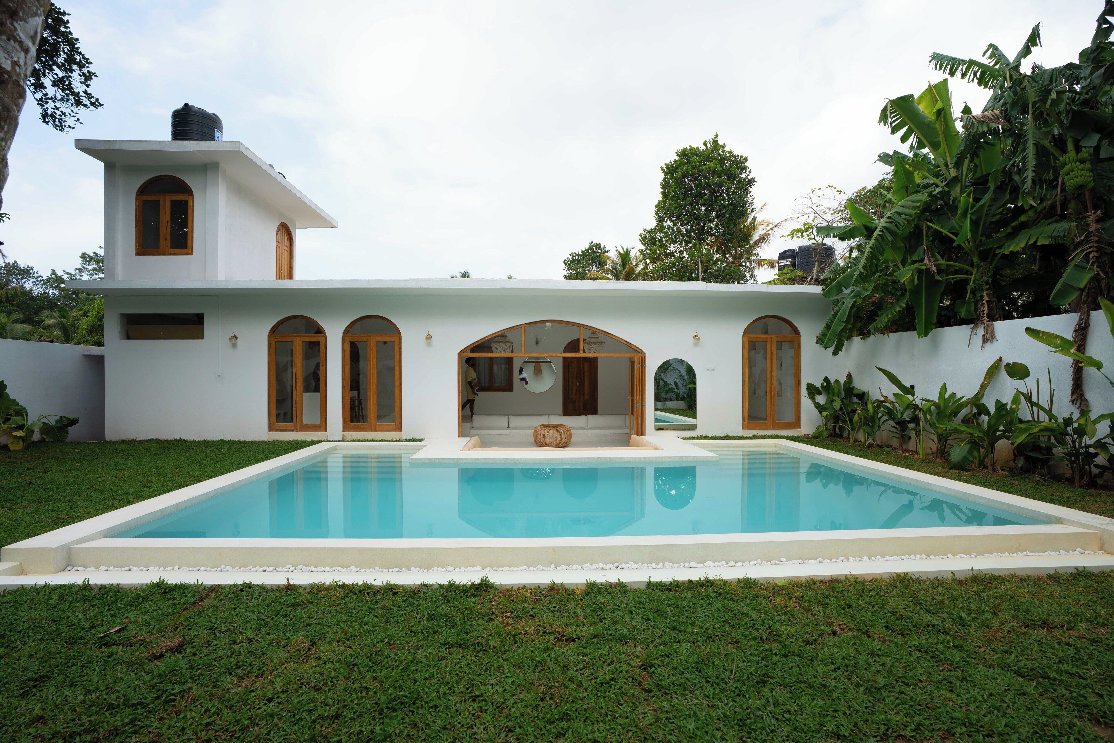 Une maison moderne dotée d’une piscine, de fenêtres en arc de cercle et d’un petit jardin.