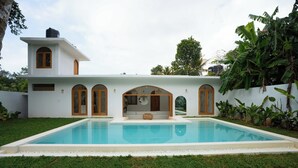 Ein modernes Haus mit Swimmingpool, Bogenfenstern und einem kleinen Garten.