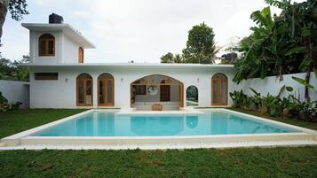 Une maison moderne dotée d’une piscine, de fenêtres en arc de cercle et d’un petit jardin.
