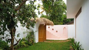 Un patio con una estructura de techo de paja, una puerta de madera y una pared blanca con una escalera.