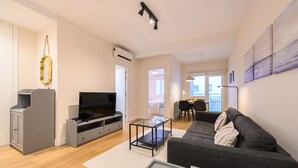 A modern living room with a grey sofa, a flat-screen TV, a coffee table, and a dining area in the background. - M Bso5 Apartamento Luminoso con 1 Dormitorio y e (Madrid)