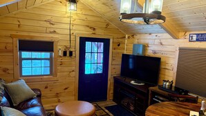 A cozy cabin interior with a wooden interior, a television, a fireplace, a dining table, and a leather sofa.
