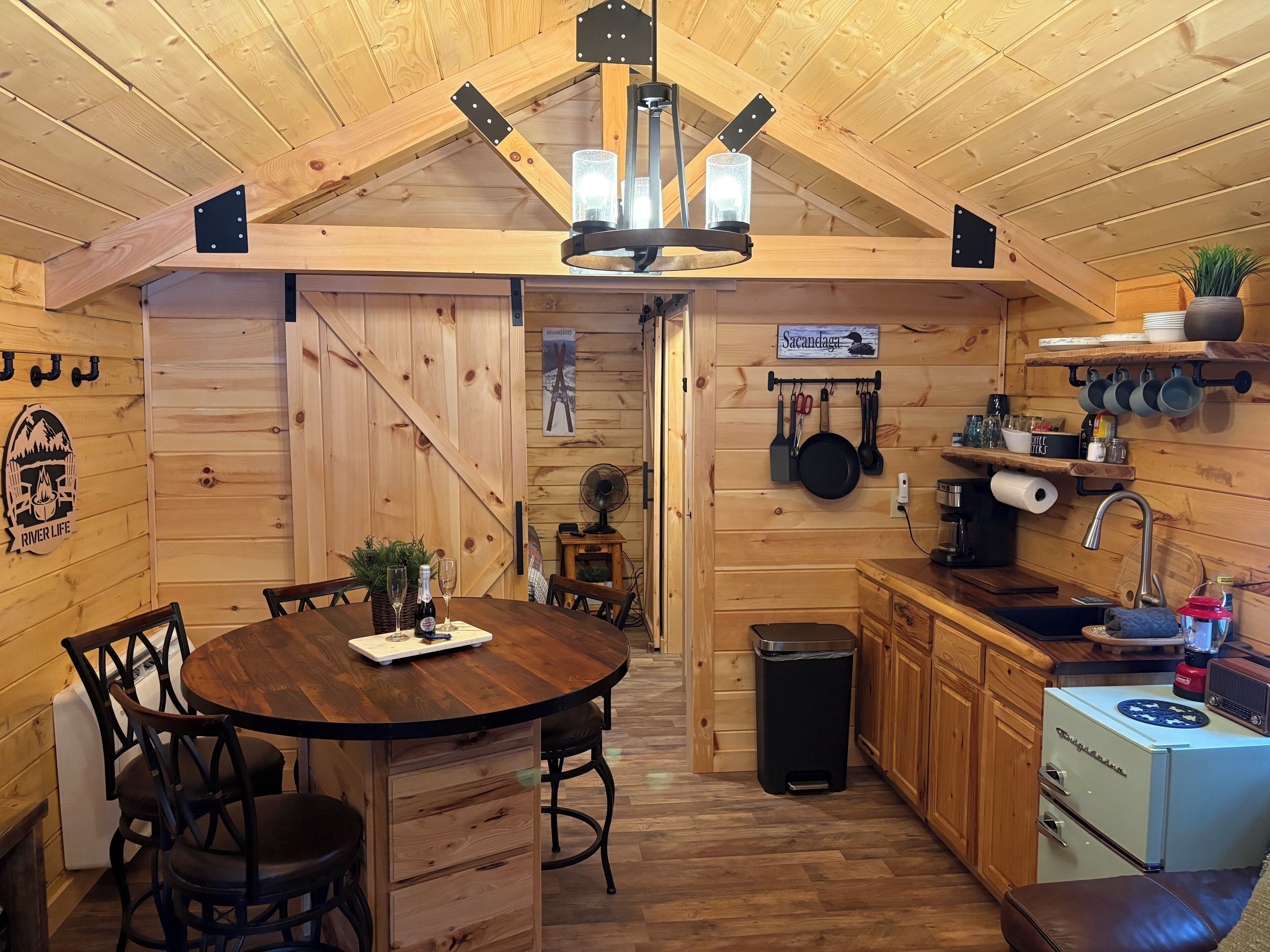 A cozy wooden cabin interior with a dining area, kitchen, and a loft bedroom.