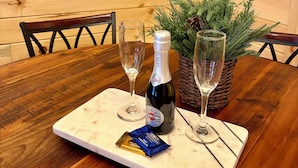 A wooden table with a bottle of Martini champagne, two glasses, and a chocolate bar.
