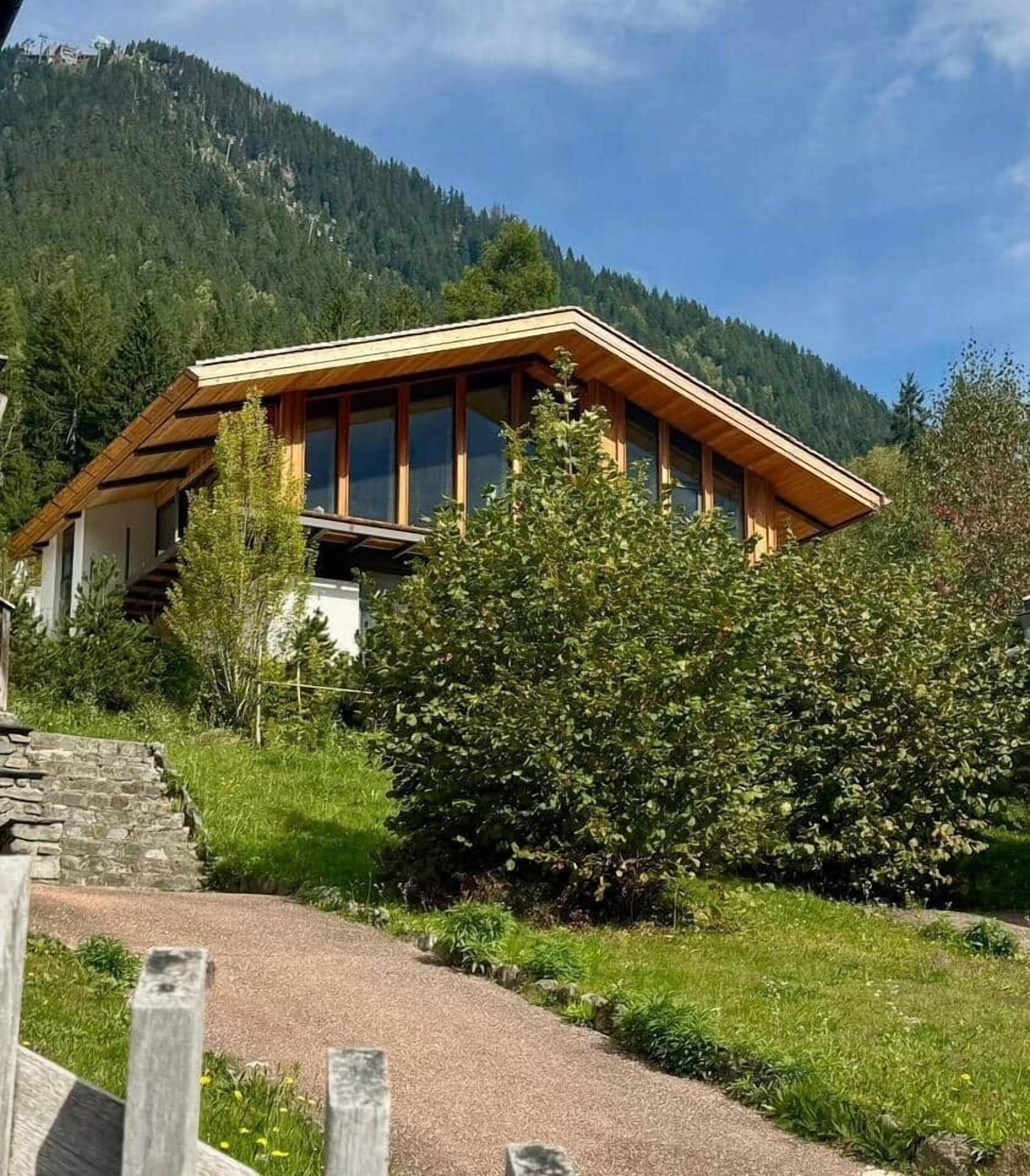 Une maison moderne avec un toit en pente, de grandes fenêtres et un chemin de pierre menant à l’entrée.
