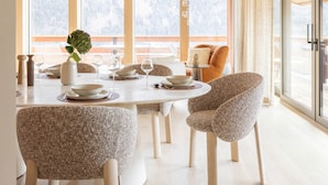 A modern dining area with a round table, chairs, and a view of snowy mountains through large windows. - Chalet Acorn 4 bedroom with SPA (Chamonix)