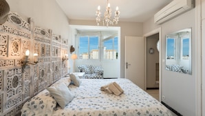 A bedroom with a patterned bedspread, a chandelier, a decorative wall panel, and a large mirror. - Marbella Center – 350m from the Beach (MARBELLA)