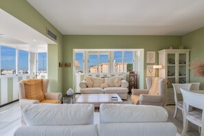 A living room with a sofa, armchairs, a coffee table, and a view through large windows.