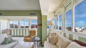 A spacious living room with a sofa, armchair, and coffee table, large windows with a city view, and a decorative lamp. - Marbella Center – 350m from the Beach (MARBELLA)