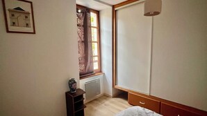 Ein Schlafzimmer mit Bett, Heizkörper, einem Fenster mit Vorhängen, einem gerahmten Bild an der Wand und einem hölzernen Kopfteil.