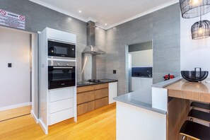 A modern kitchen with built-in ovens, a stainless steel range hood, and a wooden countertop. - Burmeister Circle by Ctha (Cape Town)