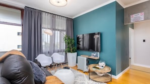 Uma sala de estar moderna com uma parede em tom de verde-água, um sofá de couro preto, cadeiras brancas, uma televisão grande e um radiador.