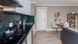 Eine moderne Küche mit schwarzem Arbeitsplatz, weißen Schränken und einer Edelstahl-Dunstabzugshaube. Es gibt einen Essbereich mit weißem Tisch und Stühlen, sowie ein Bücherregal mit Dekoration.