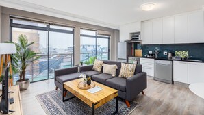 Ein modernes Wohnzimmer mit einem grauen Sofa, einem Holztisch und einem großen Fenster mit Blick auf die Stadt.
