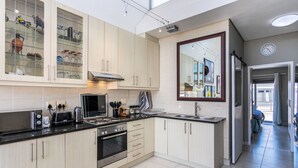 A modern kitchen with light wood cabinets, a black countertop, stainless steel appliances, and a large window providing natural light. - Seaside Village J9 by Ctha (Cape Town)