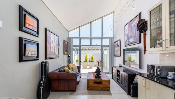 A modern living room with a large window, a sofa, a coffee table, and a guitar leaning against the wall. - Seaside Village J9 by Ctha (Cape Town)
