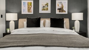 A modern bedroom with a large bed, two bedside tables with lamps, and three framed landscape paintings on the wall. - Rockwell 220 by Ctha (Cape Town)