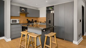 A modern kitchen with grey cabinets, a stainless steel refrigerator, a microwave, wooden stools, and a wooden countertop. - Rockwell 220 by Ctha (Cape Town)