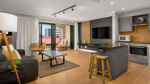 A modern apartment with a kitchen, dining area, and living room. It features a large island, a flat-screen TV, and a microwave. - Rockwell 220 by Ctha (Cape Town)