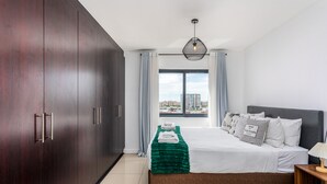A modern hotel room with a large bed, a wardrobe, a window with curtains, and a city view. - Knightsbridge 702w by Ctha (Cape Town)