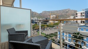 Ein Balkon mit Korbmöbeln, der auf einen Stadtblick mit einem Berg im Hintergrund blickt.