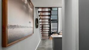 Ein modernes Interieur mit einem großen gerahmten Bild an der Wand, einer Holztreppe und einer Küchenzeile mit Arbeitsplatte und Spüle.
