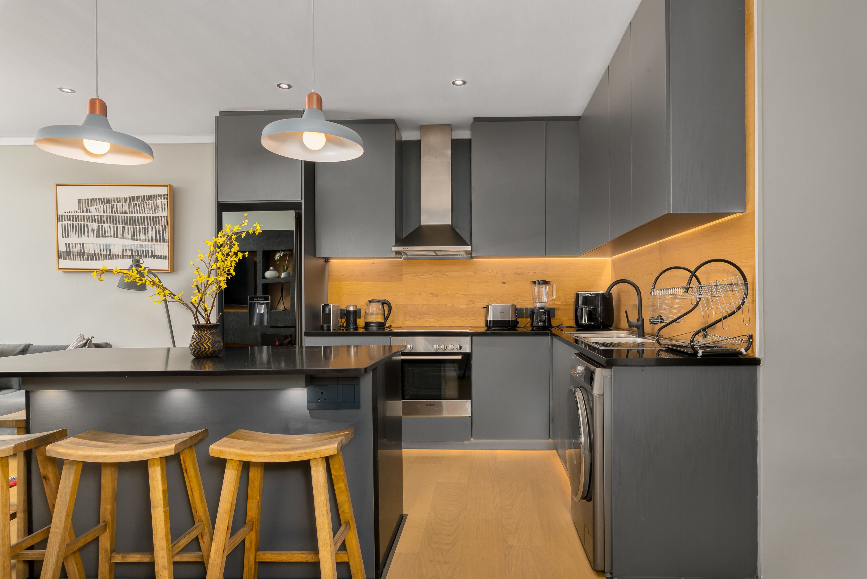 Une cuisine moderne avec des meubles de couleur grise, des tabourets en bois, un îlot central et des luminaires suspendus.