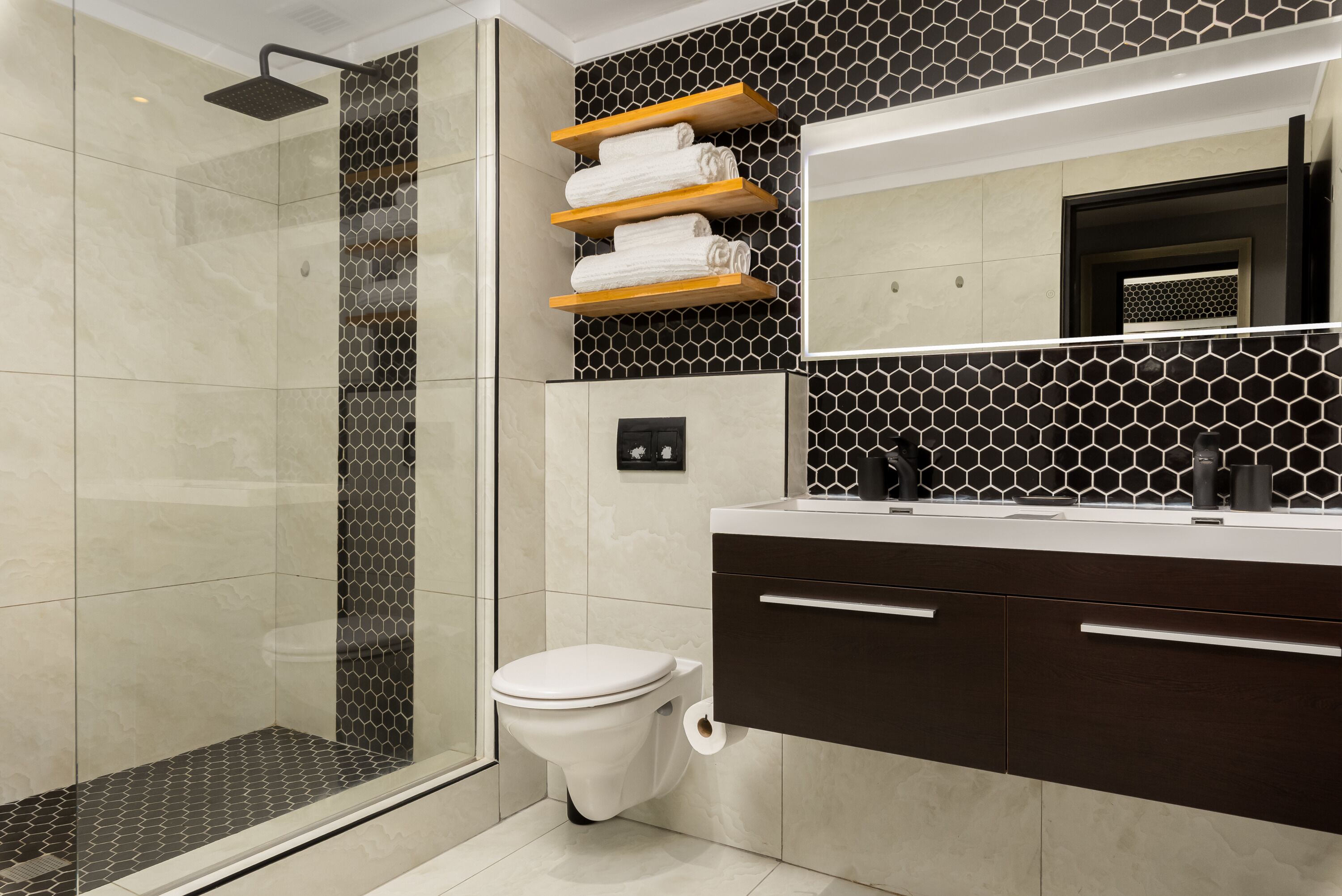 A modern bathroom with a glass-enclosed shower, a toilet, and a vanity with a mirror and towel racks.