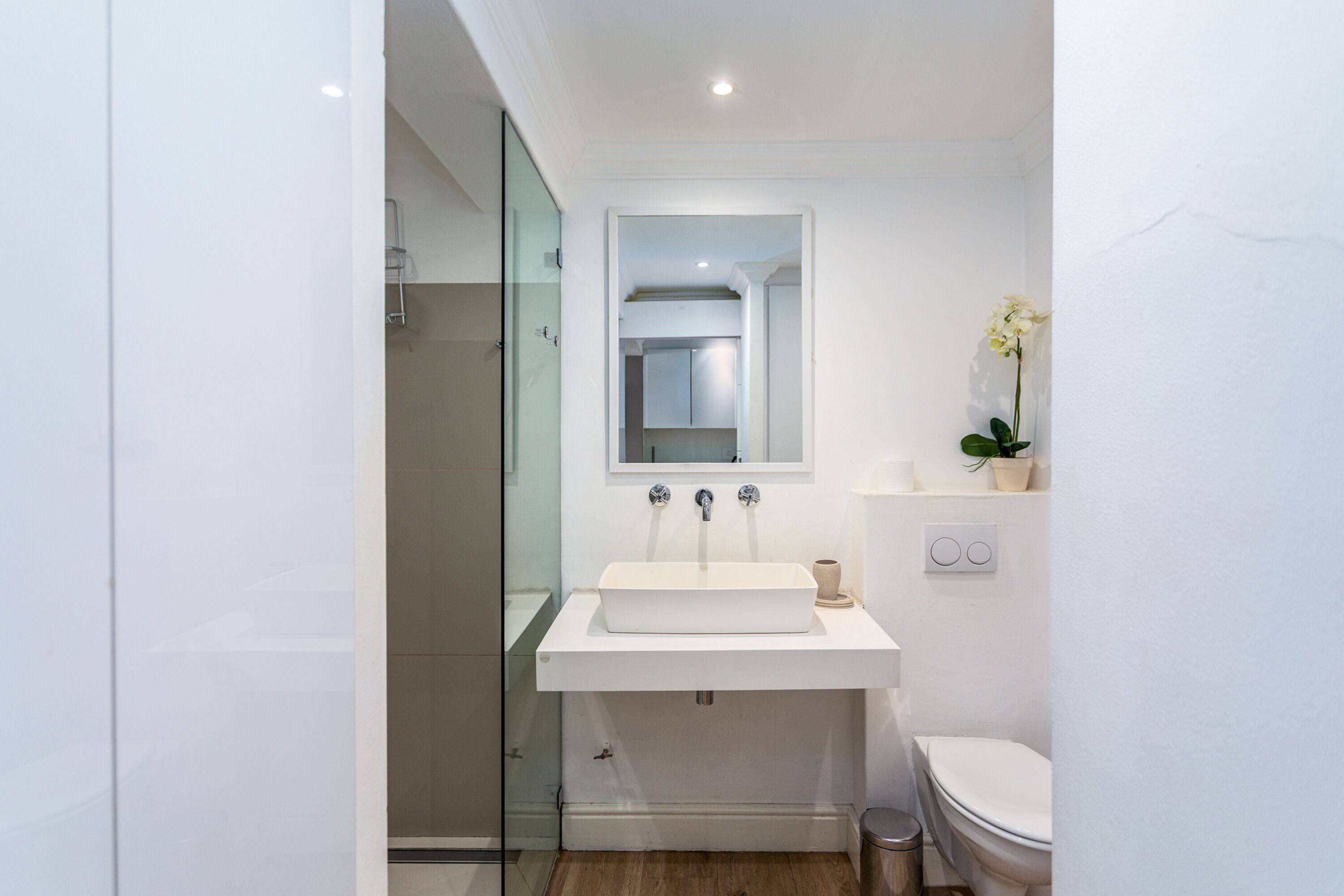 A modern bathroom with a glass shower enclosure, a white sink with a mirror above it, and a toilet.