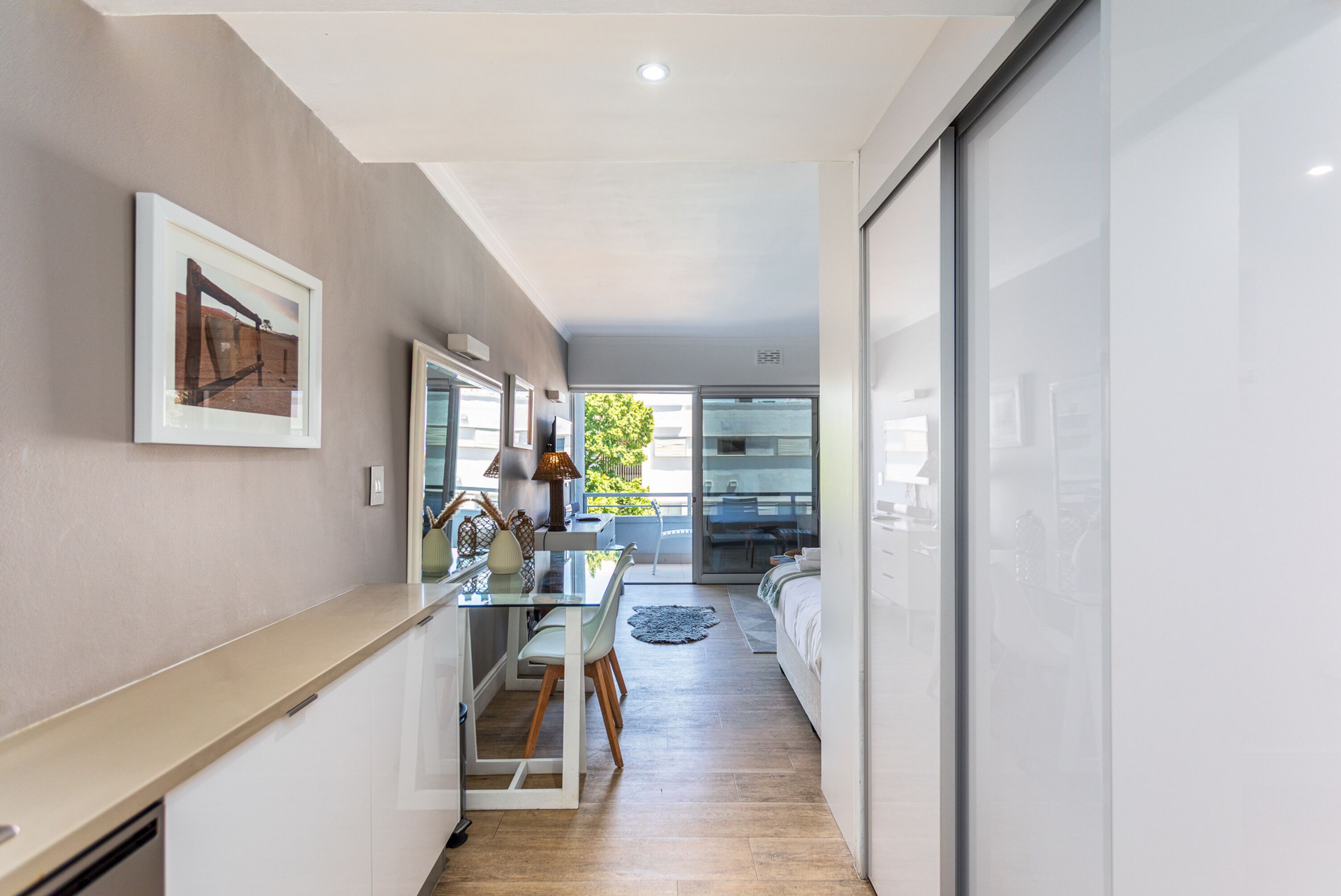 Um corredor estreito com uma cozinha, uma mesa de jantar e uma cama no quarto adjacente.