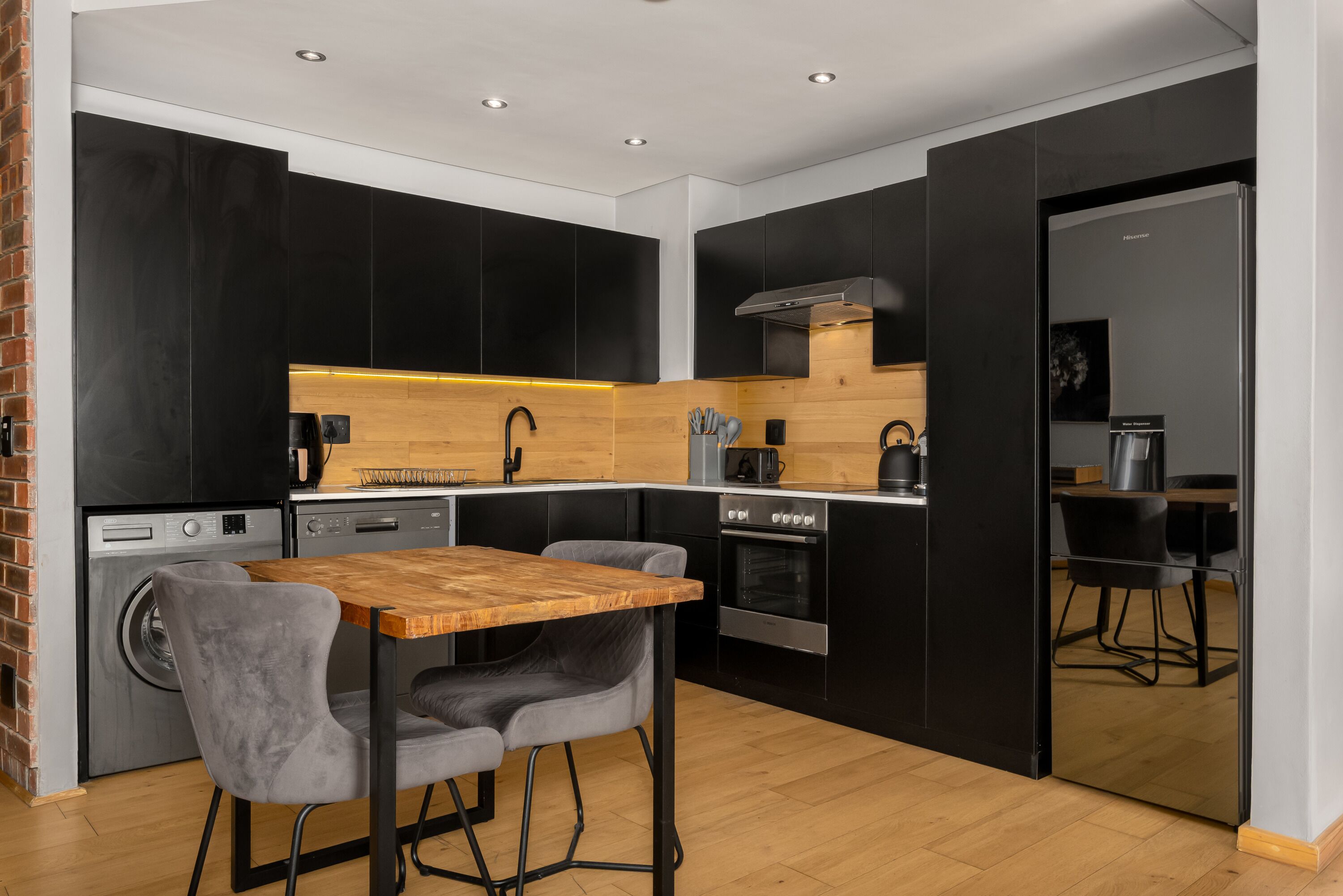 A modern kitchen with black cabinets, a wooden table, and a grey upholstered chair.