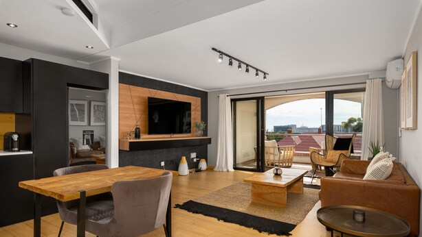 A modern living room with a wooden dining table, grey chairs, a sofa, and a TV mounted on the wall. - Rockwell 221 by Ctha (Cape Town)