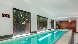 A long indoor swimming pool with clear glass walls, large windows, and a wooden wall with a clock. - Rockwell 221 by Ctha (Cape Town)