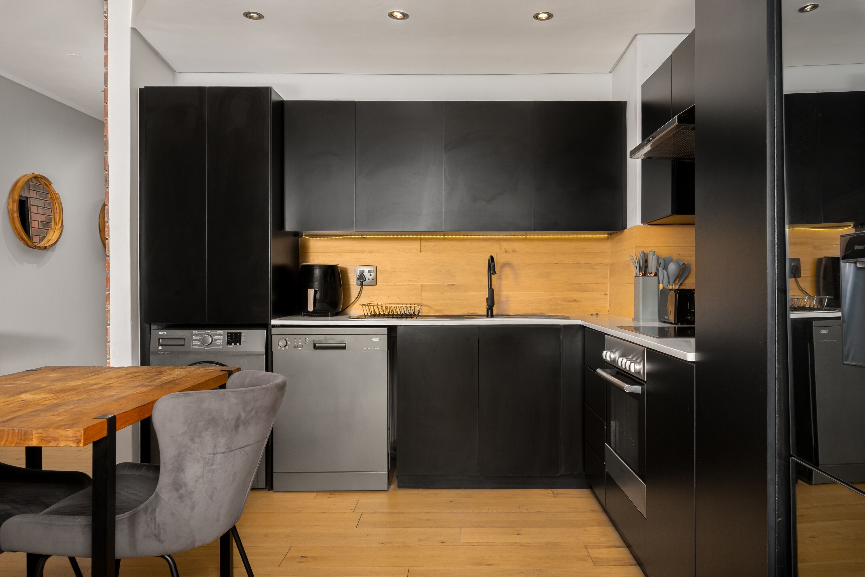 Una cocina moderna con armarios negros, encimera de madera y lavavajillas.