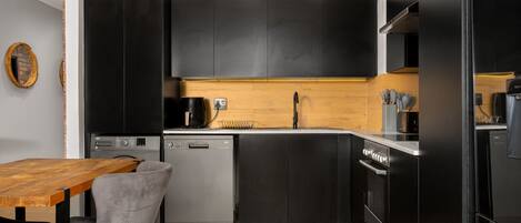 Una cocina moderna con armarios negros, encimera de madera y lavavajillas.