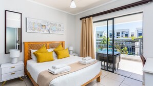 Habitación de hotel con cama, mesita de noche, lámpara, cuadro, balcón con mesa y sillas, y vistas a edificios.