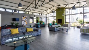Un hall espacioso con mobiliario moderno, ventanas amplias y un techo alto con vigas a la vista.