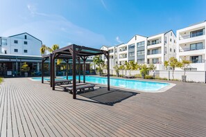 Eine Holzterrasse mit Pool, einem Gazebo und modernen Gebäuden im Hintergrund.
