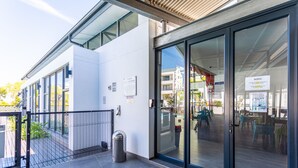 Un edificio moderno con amplios ventanales, una cerca de metal y un contenedor de basura.